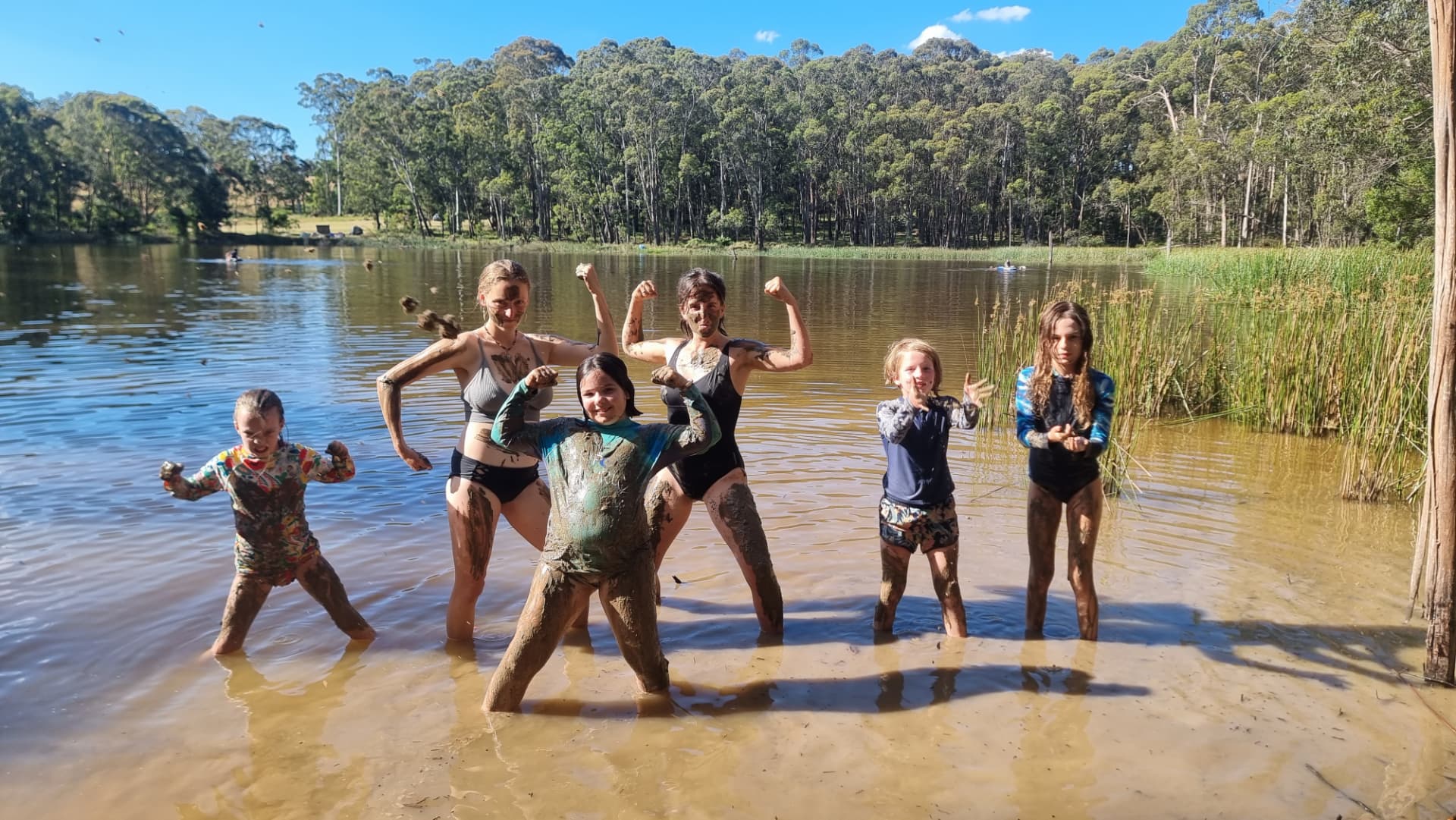 Kids covered in mud flexing in the shallows of the lake
