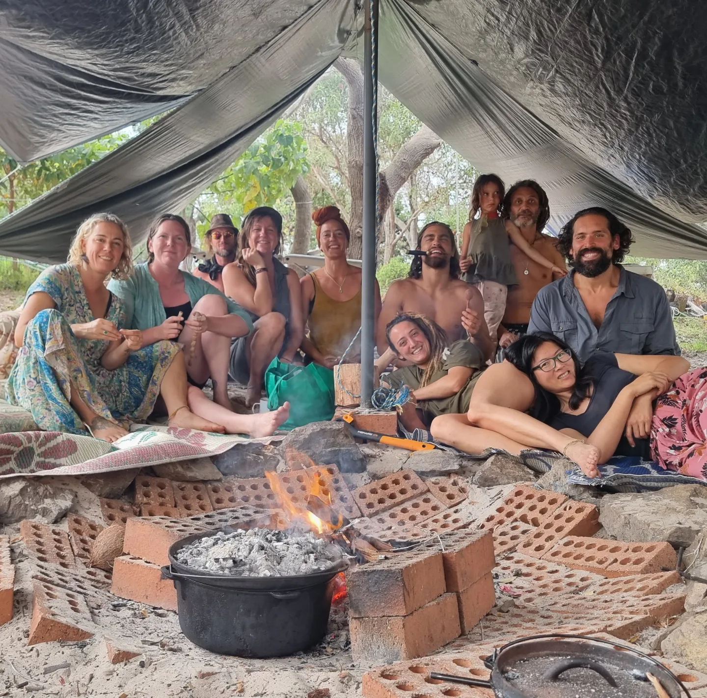 The crew gathered under a tarp around the camp oven at a campout