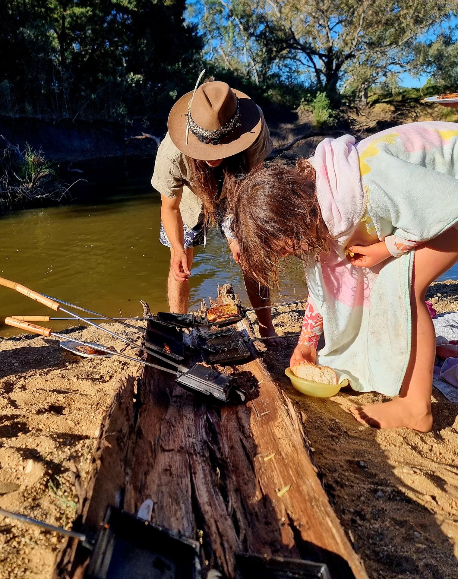 Cooking jaffles on the coals beside the river with a child helping