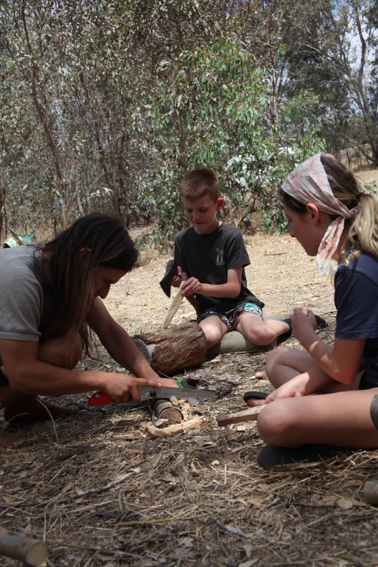 Children and a mentor sawing wood together on the ground