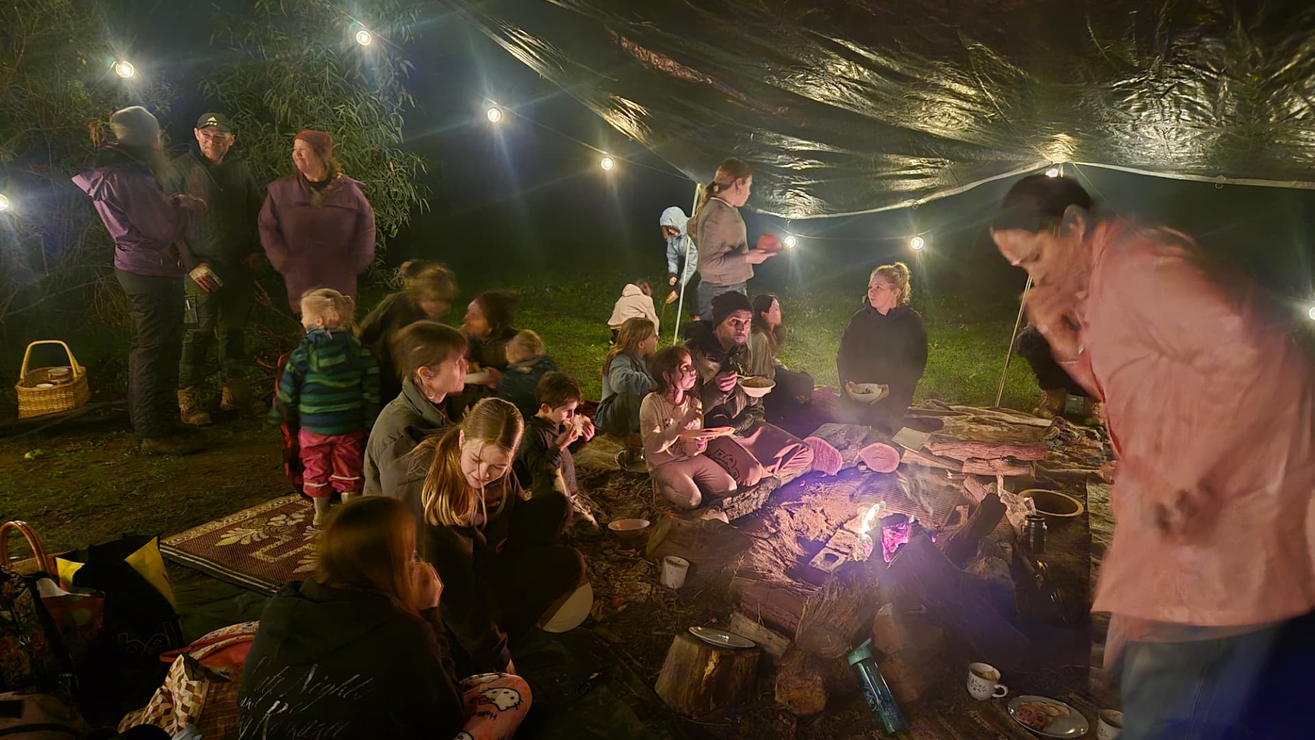The community sharing a meal around the fire under lights at solstice