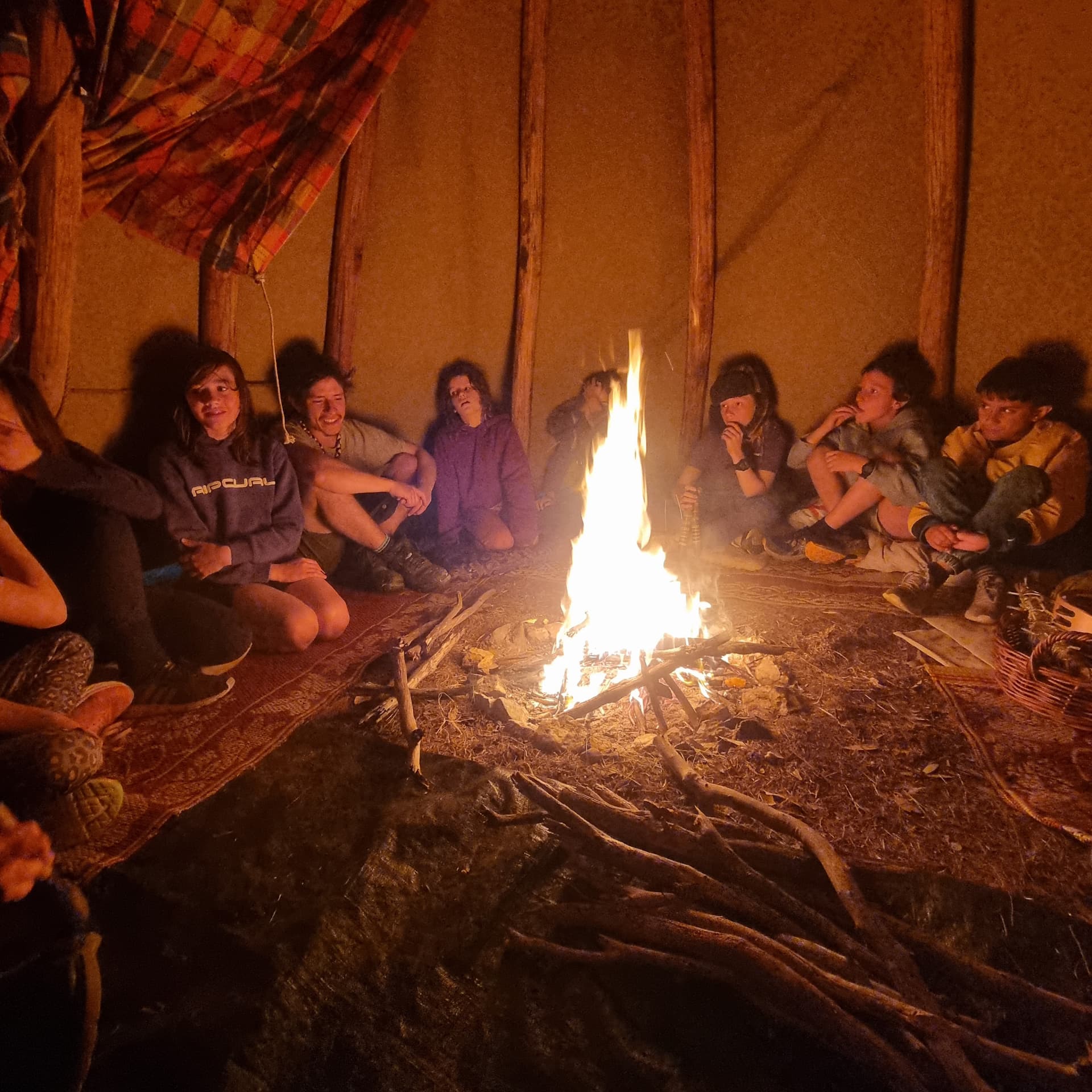 Kids sitting around a crackling fire at night inside the cob building