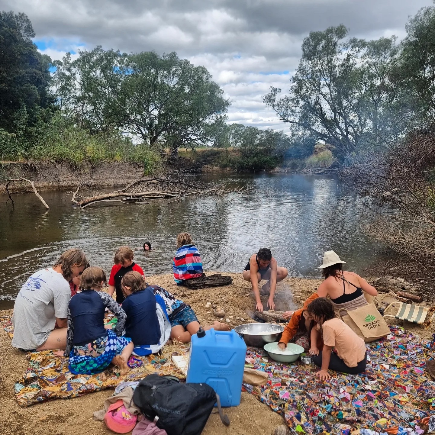 Kids swimming and cooking on the sand beside the river