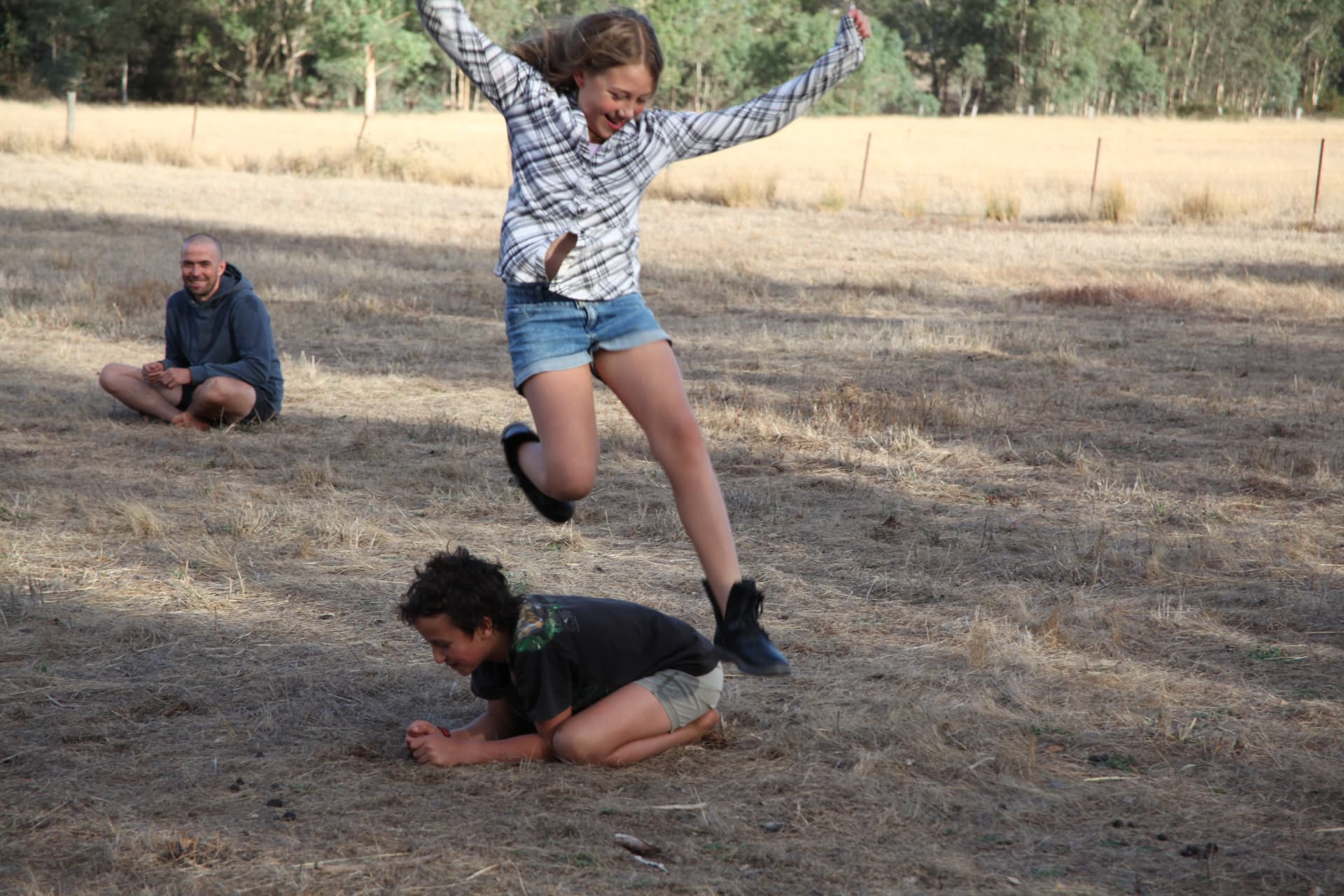 A young person leaping over a friend in a sunny grassy field