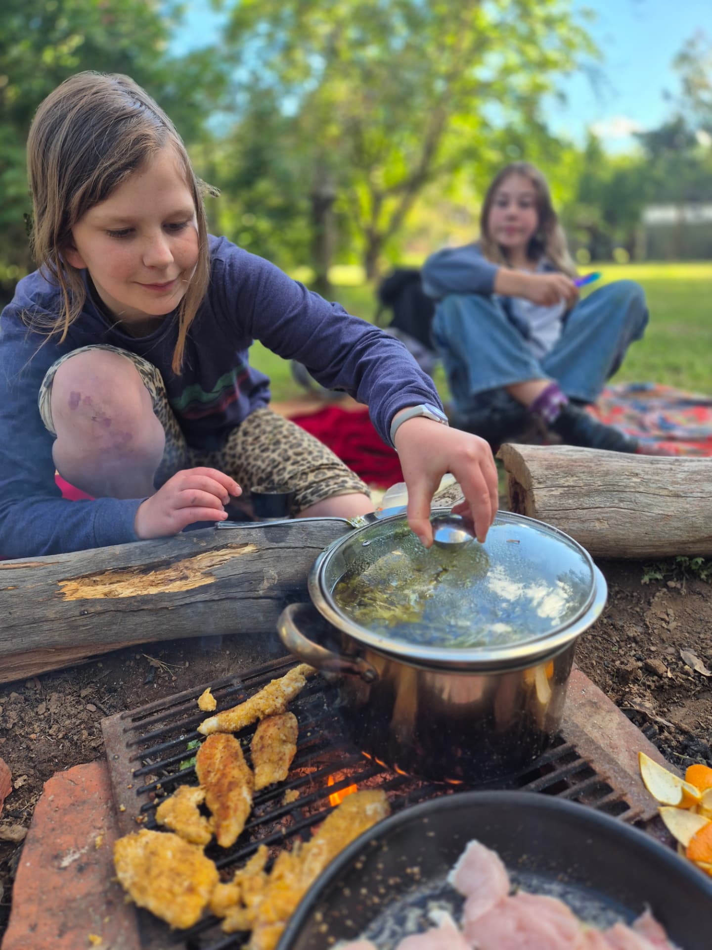 A young person cooking food over an open campfire