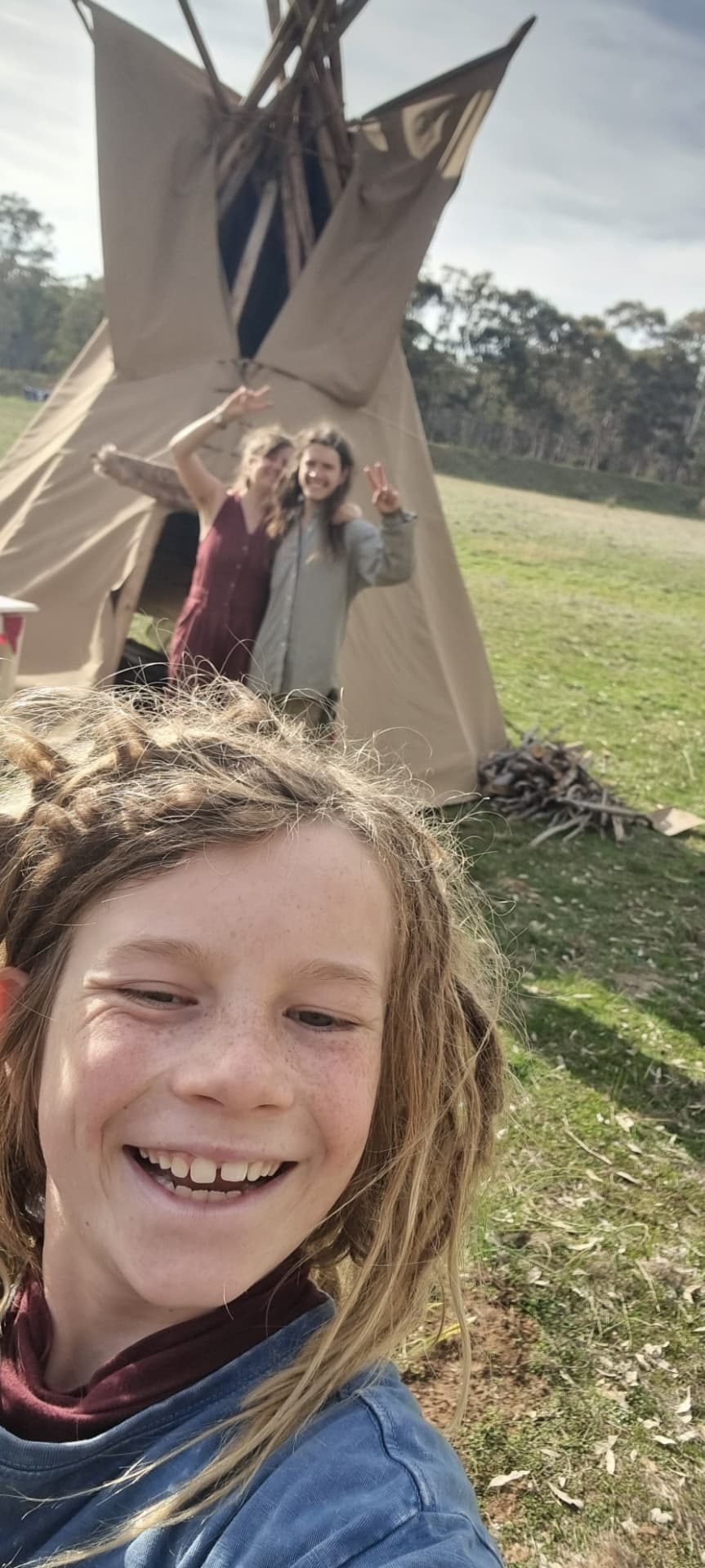 A grinning child taking a selfie in front of the tipi