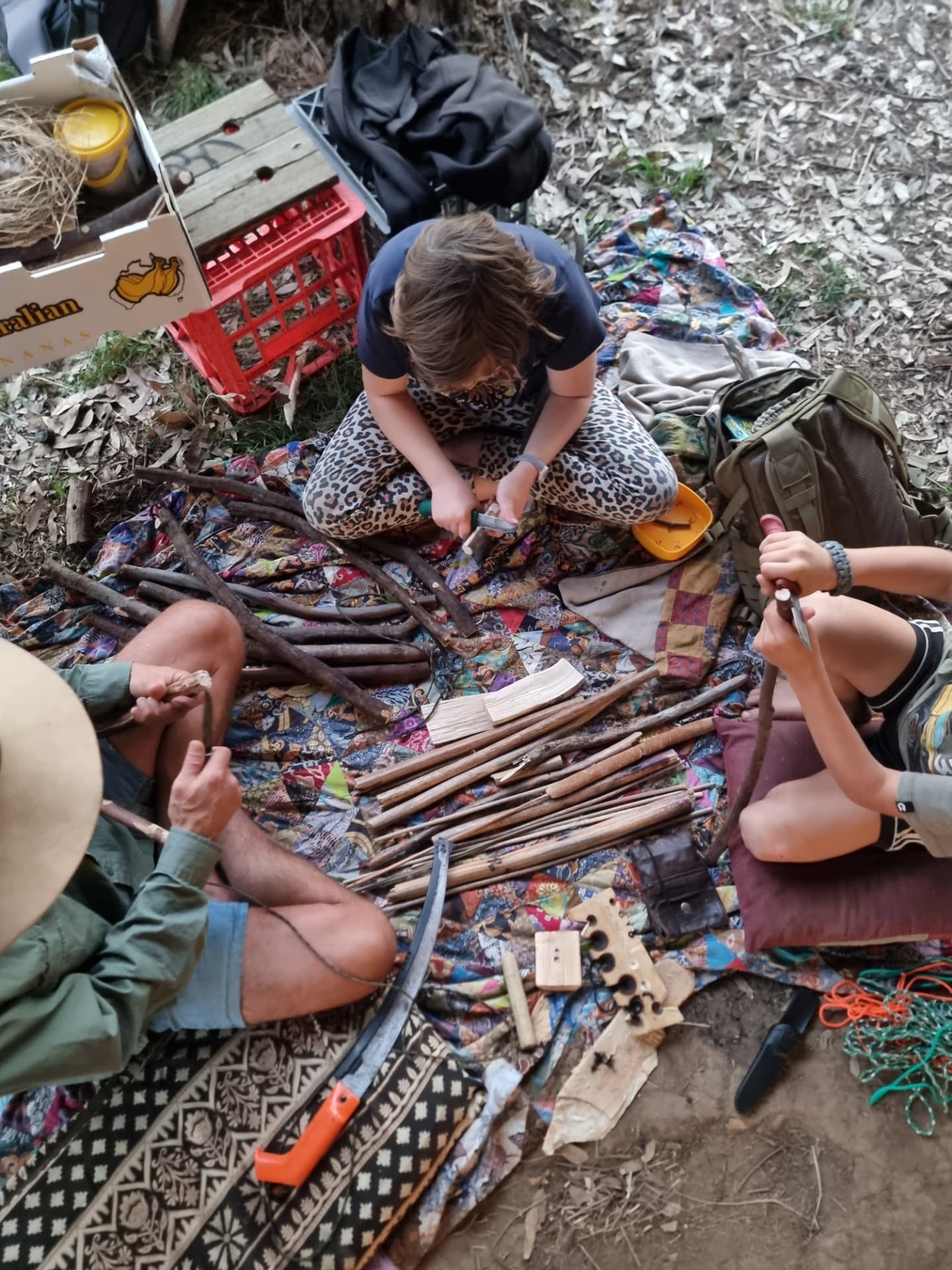 Children and a mentor practising carving and tool skills together on a picnic rug