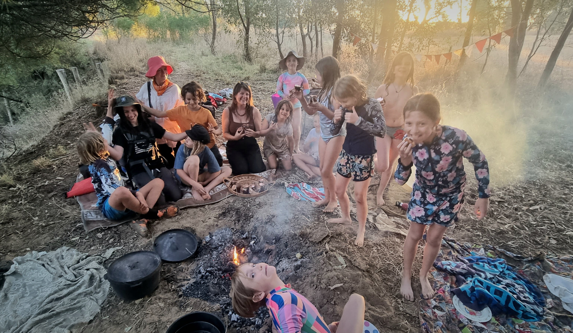 Families sharing dinner around the fire at sunset at a campout