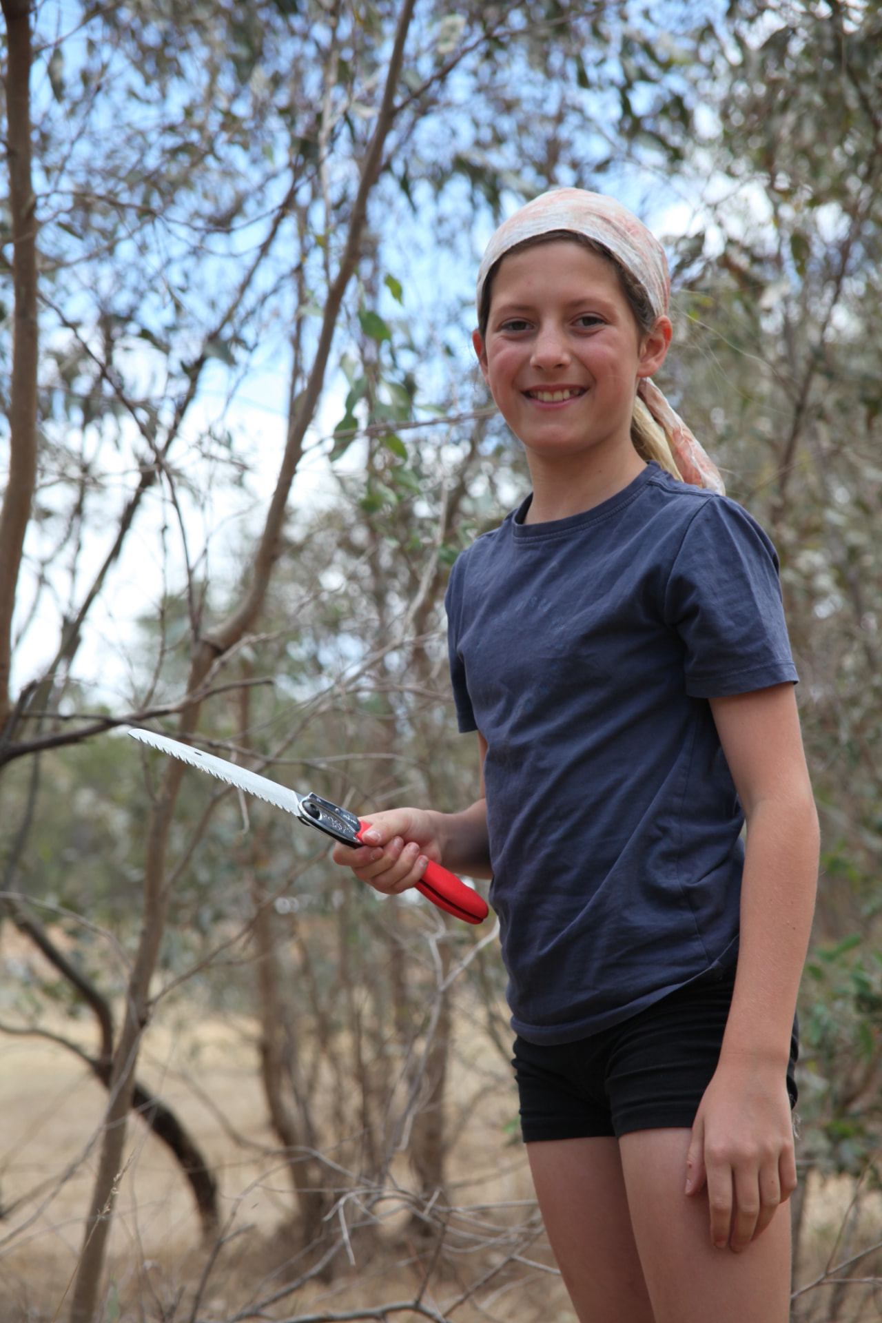 A young person holding a folding saw in the bush